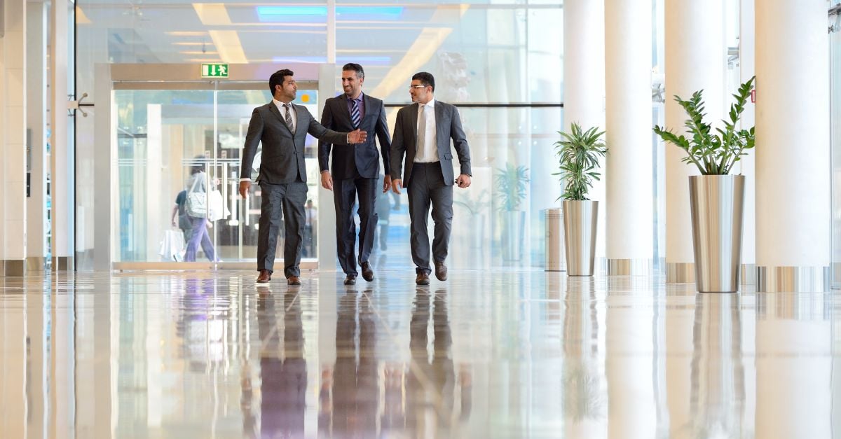 Three businessmen walking side by side discussing outsourcing their global payroll responsibilities