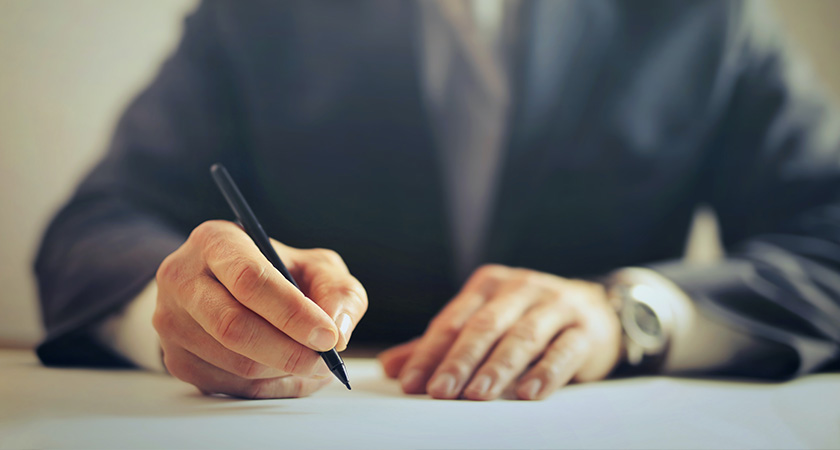 Close up of a businessman’s hands writing something UK payroll process related on a document.