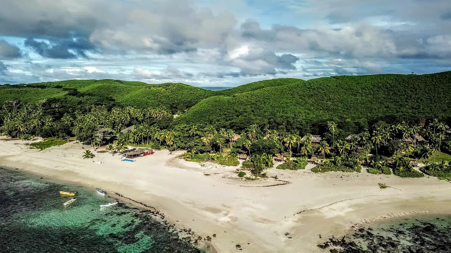 Aerial view of a palm-fringed white sand beach and turquoise reef in Fiji