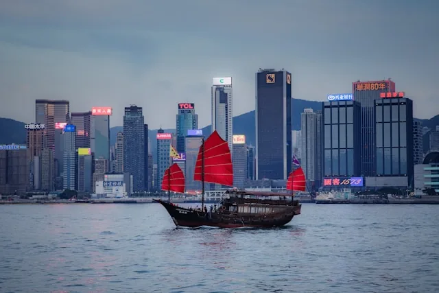 A traditional red-sailed junk boat crossing Victoria Harbour against the Hong Kong skyline