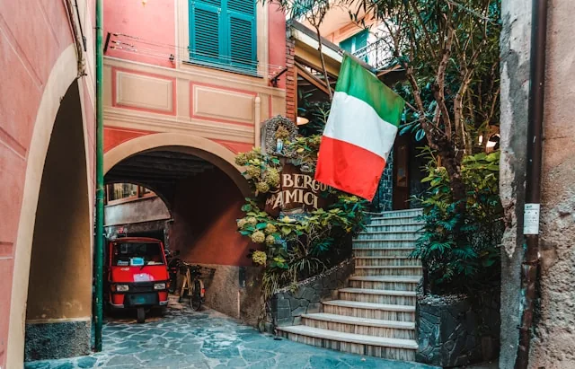 An Italian flag over a narrow village street with a classic red Ape, Italy