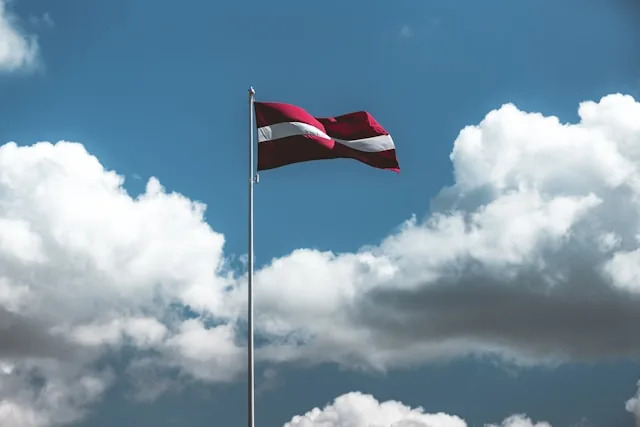 The Latvian flag flying against a blue sky with clouds, Latvia
