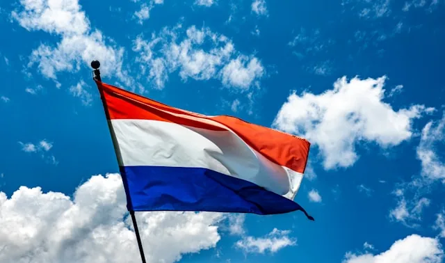 The Dutch national flag flying against a blue sky