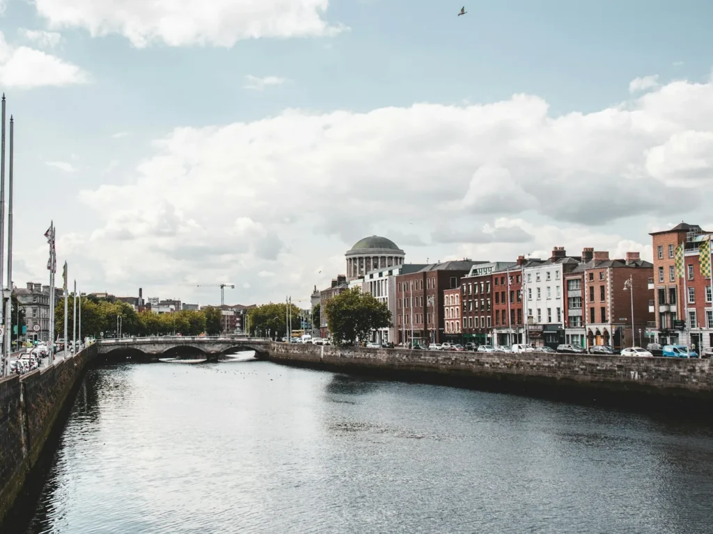 Quayside buildings along the north bank of the River Liffey in Dublin, brick and rendered facades above ground-floor shops with traffic on the quay and the dome of the Four Courts behind, Dublin, Ireland