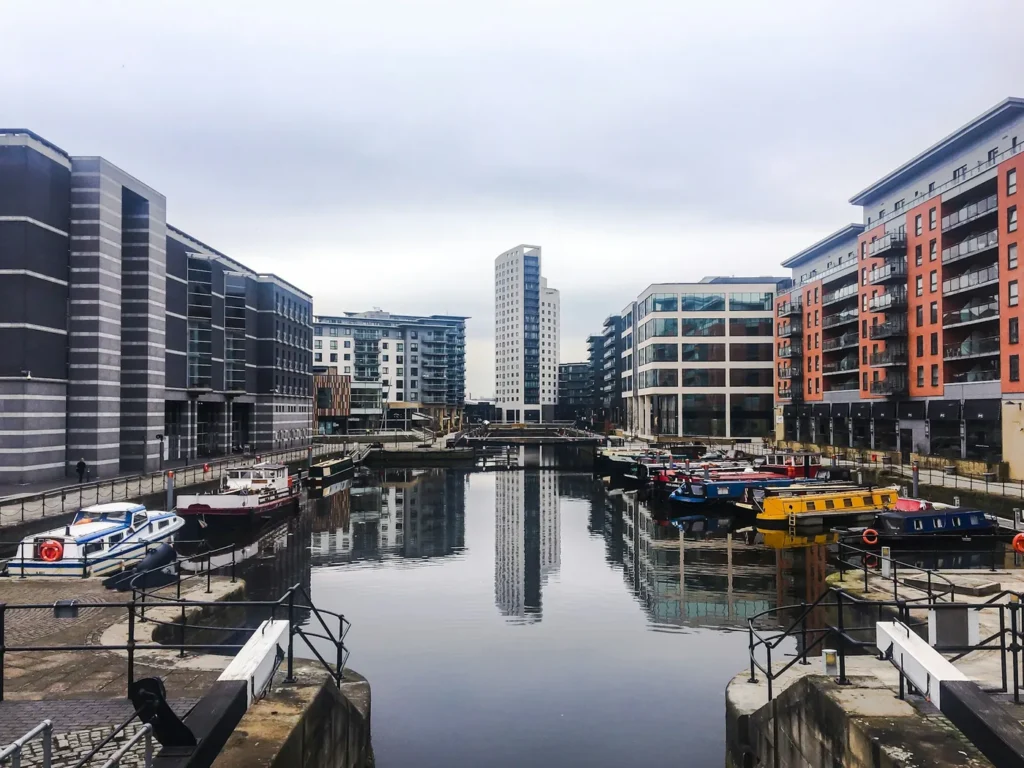 Leeds Dock on an overcast day, with waterside offices and apartments along both quays, narrowboats moored at the edge of the water and the buildings reflected in still water, Leeds, United Kingdom
