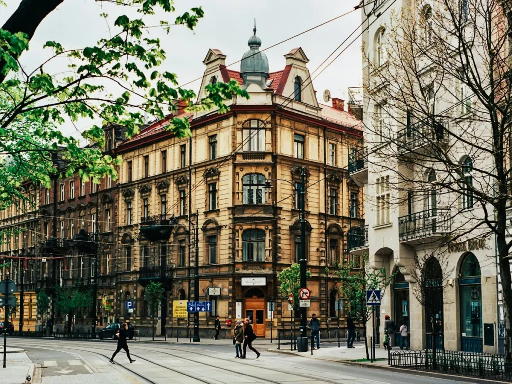 A domed corner tenement on a tree-lined street with tram tracks in Kraków, Poland
