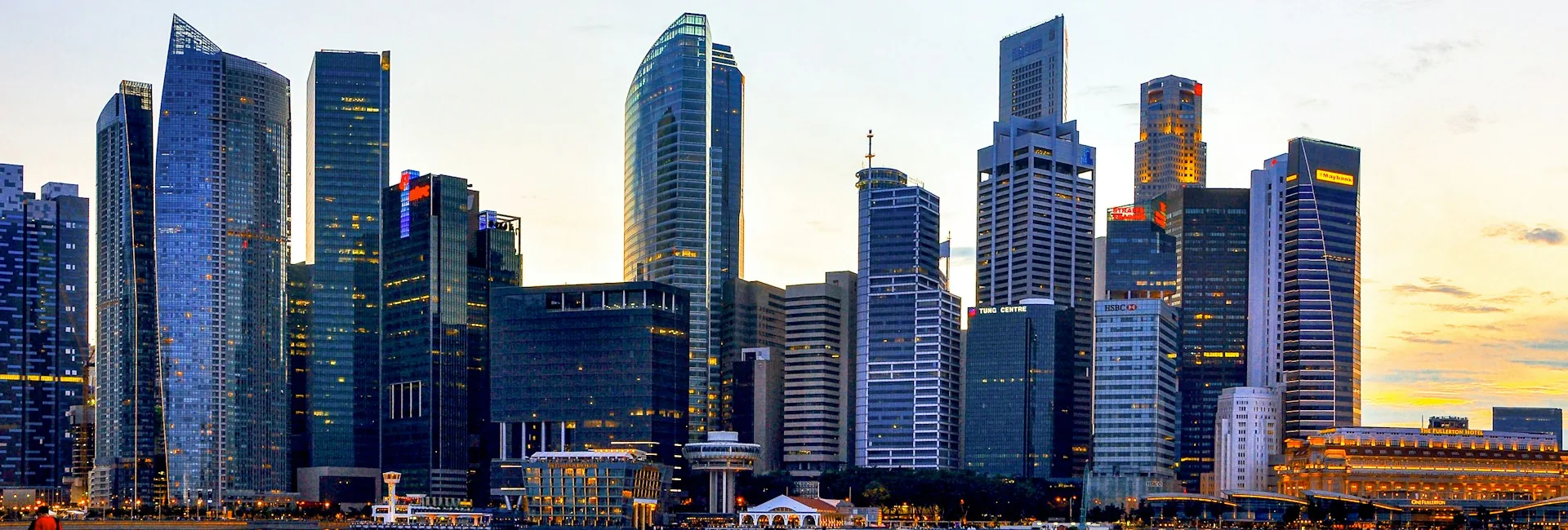 Office towers of Raffles Place in the Singapore central business district at dusk, seen across Marina Bay, with lights coming on in the buildings and the waterfront below, Singapore