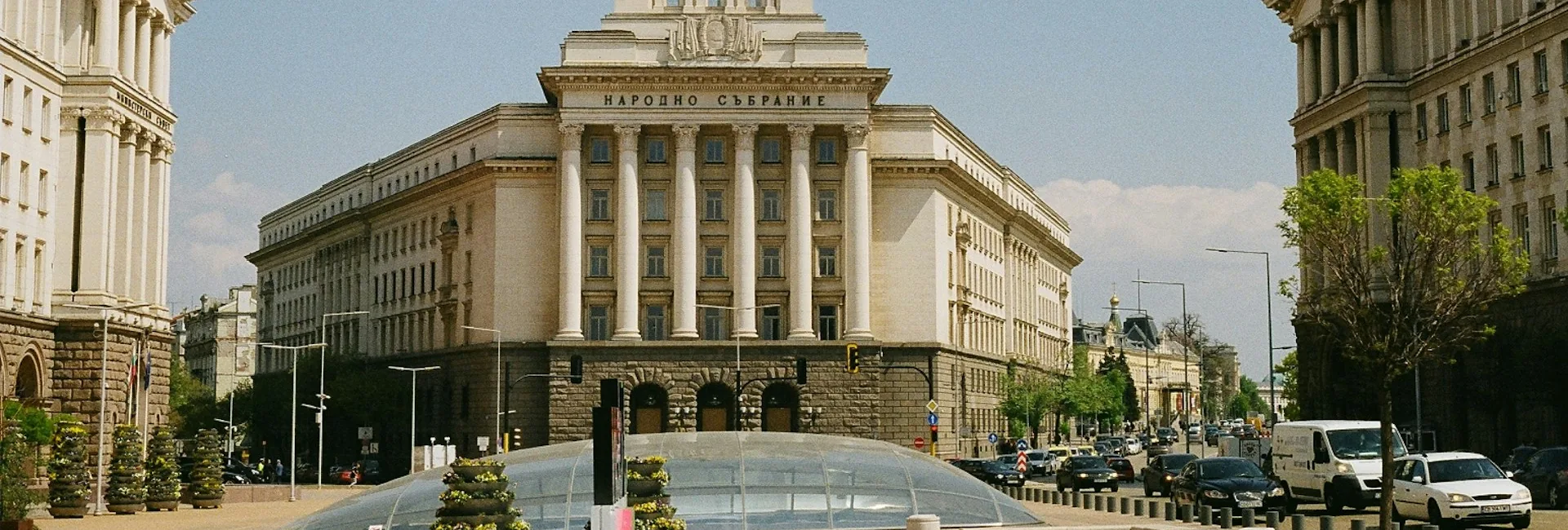 The Largo in central Sofia, with the colonnaded government buildings on both sides of the boulevard, traffic along the avenue and the glass dome of the Serdika metro entrance in the foreground, Sofia, Bulgaria