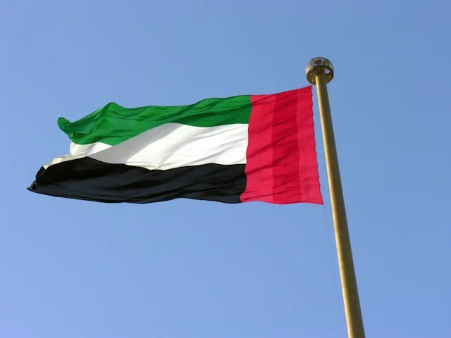 The flag of the United Arab Emirates flying from a pole against a clear blue sky