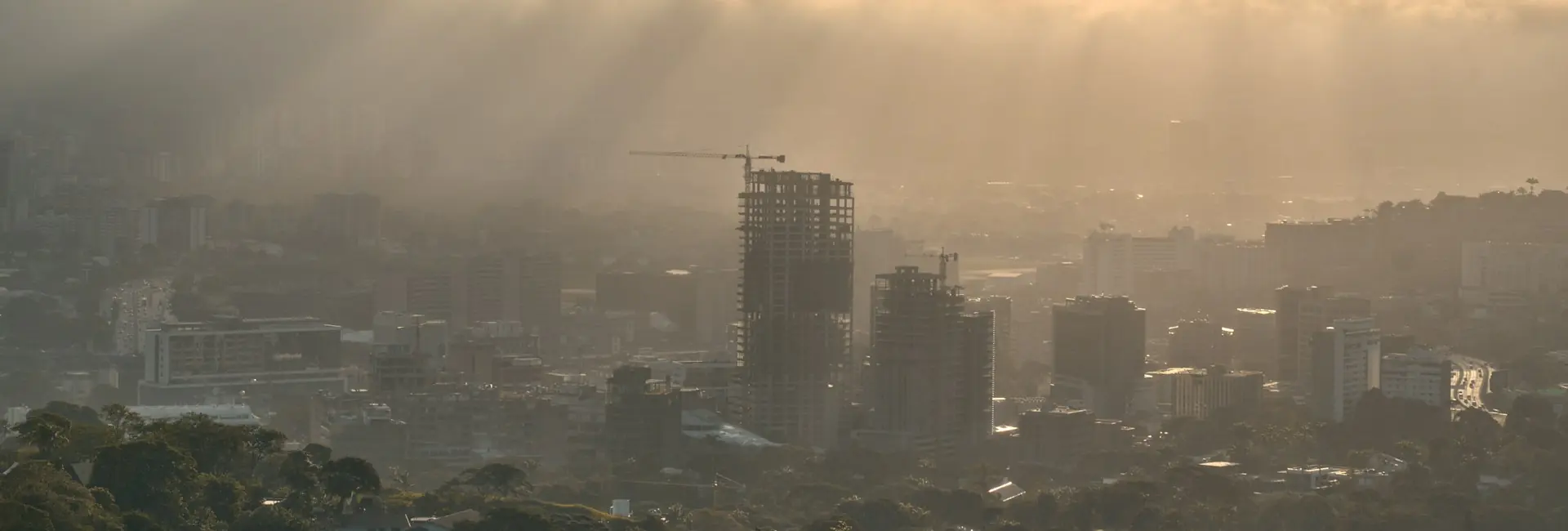 The Caracas skyline at sunrise, with towers under construction and sun rays through the clouds, Venezuela