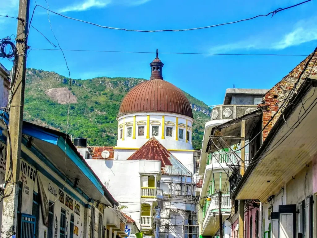 The dome of the Cap-Haïtien cathedral above a street of colourful houses, with green mountains behind, Haiti