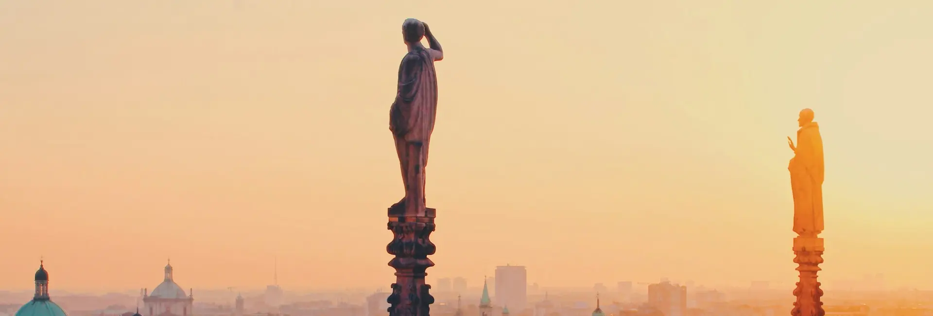 Statues on the spires of Milan Cathedral above the rooftops and domes of the city at sunset, Milan, Italy