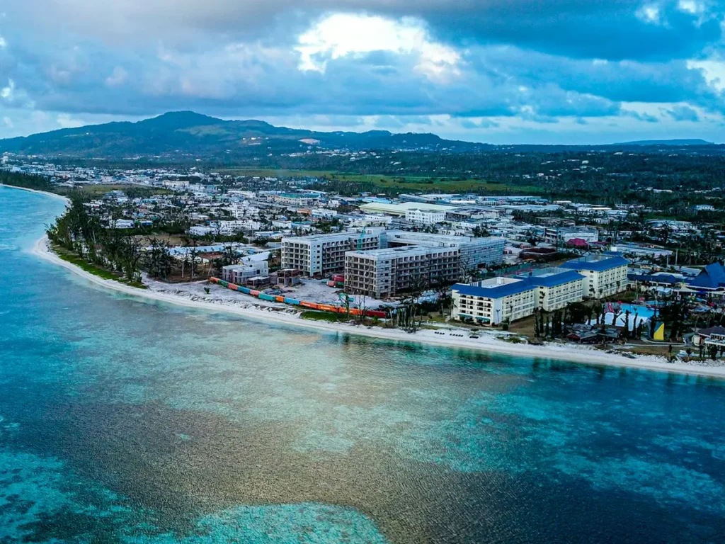 Buildings beside a white sand beach on Saipan with the hills of the island behind, Northern Mariana Islands